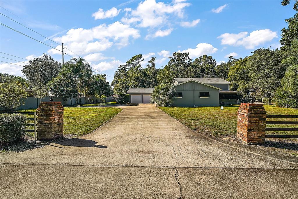 A concrete driveway leads to a house and detached garage behind two brick pillars — 1661 VOTAW ROAD, APOPKA, FL