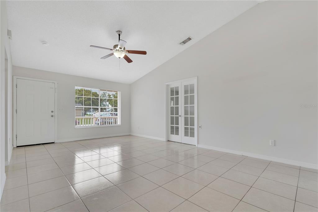 A bright room with vaulted ceilings, white tile floors, a ceiling fan, and French doors — 9249 SPRING VALE ROAD, ORLANDO, FL