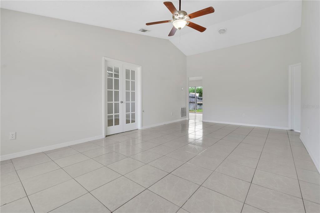 An empty room with light-colored tile flooring, a vaulted ceiling, and white French doors — 9249 SPRING VALE ROAD, ORLANDO, FL