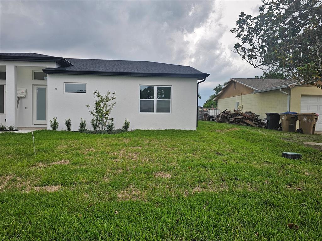 A white house with a dark roof stands next to a neighboring property with debris — 292 GARDENIA ROAD, KISSIMMEE, FL