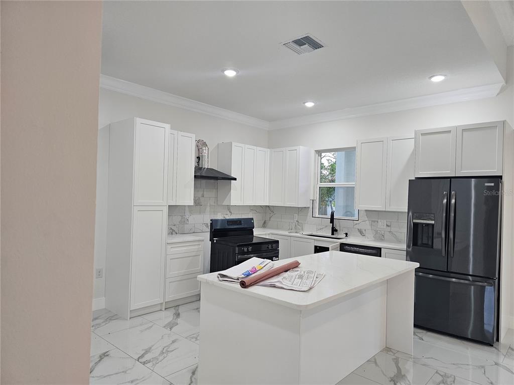 A modern kitchen features white cabinets, marble-look tile floors, a center island, and black appliances — 292 GARDENIA ROAD, KISSIMMEE, FL