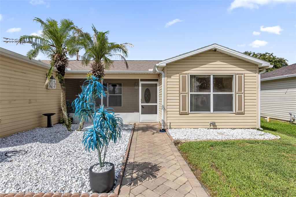 A tan, single-story house features a stone walkway, white gravel landscaping, and a palm tree — 17648 SE 93RD BUTLER COURT, THE VILLAGES, FL