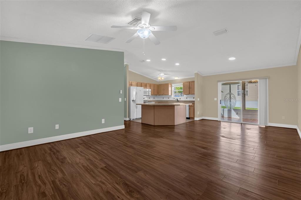 An open-concept living area features dark wood-look flooring, a sage green wall, and a kitchen — 17648 SE 93RD BUTLER COURT, THE VILLAGES, FL