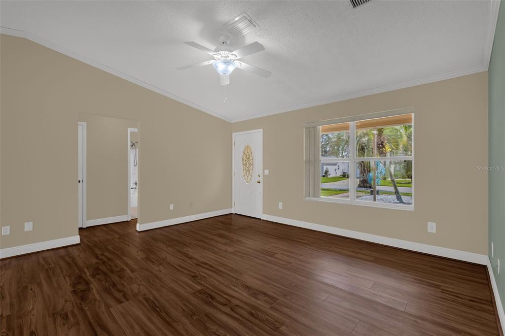 An empty living room with wood-look flooring, a ceiling fan, and a white front door — 17648 SE 93RD BUTLER COURT, THE VILLAGES, FL