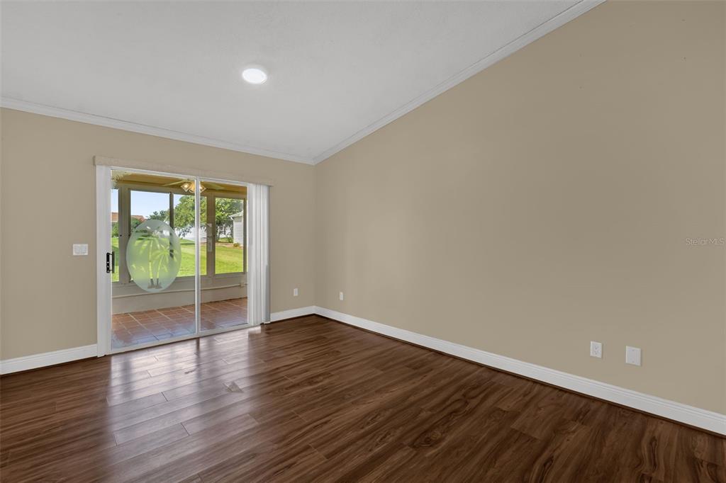 An empty room with wood-look flooring, beige walls, and a sliding glass door to a patio — 17648 SE 93RD BUTLER COURT, THE VILLAGES, FL