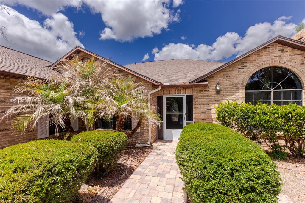 A brick house exterior features a stone walkway leading to a front door with shutters — 14692 LINDEN DRIVE, SPRING HILL, FL