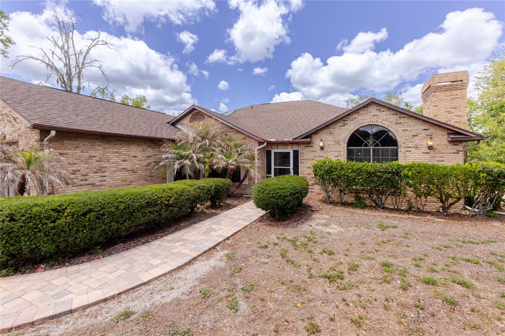 A brick house exterior features a paved walkway leading to the front entrance and chimney — 14692 LINDEN DRIVE, SPRING HILL, FL