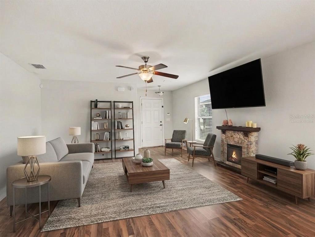 A living room features a stone fireplace, wood flooring, a ceiling fan, and virtual staging — 3057 GRAND PRESERVE BOULEVARD, MULBERRY, FL
