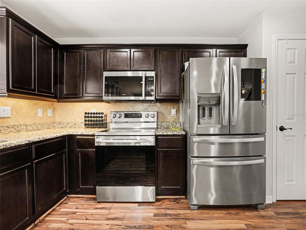 A kitchen features dark wood cabinets, granite countertops, stainless steel appliances, and wood-look flooring — 3057 GRAND PRESERVE BOULEVARD, MULBERRY, FL