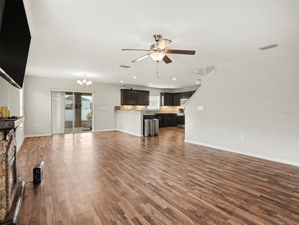 An open-concept living room and kitchen featuring wood-look flooring, dark cabinetry, and a stone fireplace — 3057 GRAND PRESERVE BOULEVARD, MULBERRY, FL