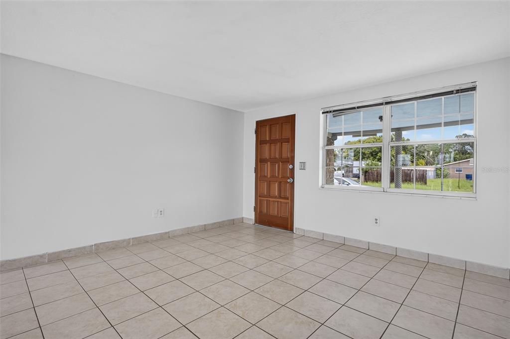 An empty room with light-colored tile flooring, white walls, a wooden door, and a window — 3852 SUNRAY DRIVE, HOLIDAY, FL