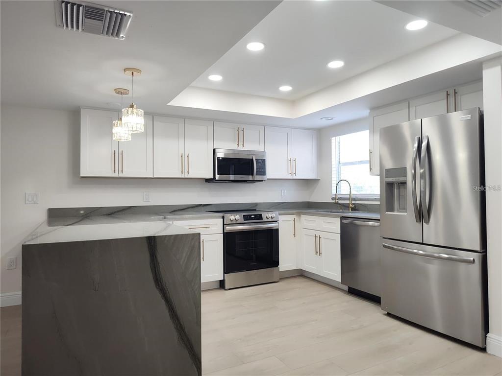 A modern kitchen features white cabinets, stainless steel appliances, and a gray waterfall island — 255 CAPRI CIRCLE N UNIT 36, TREASURE ISLAND, FL