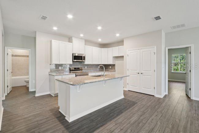 A kitchen with white cabinets, granite countertops, a center island, and wood-look flooring — 16854 NW 178TH TERRACE, ALACHUA, FL
