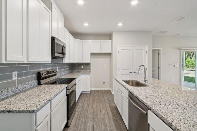 A modern kitchen features white cabinets, granite countertops, stainless steel appliances, and gray tile backsplash — 16854 NW 178TH TERRACE, ALACHUA, FL
