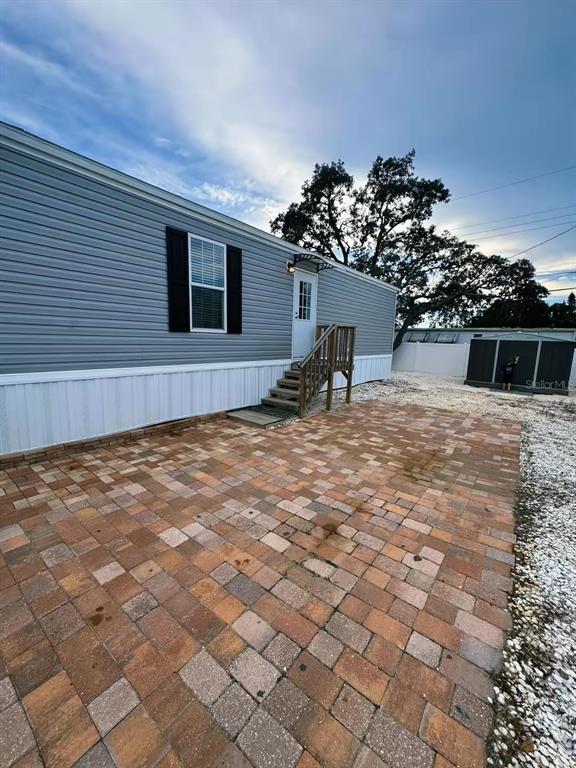 A side view of a manufactured home with gray siding, black shutters, and wooden stairs — 2013 KEPNER DRIVE, HOLIDAY, FL