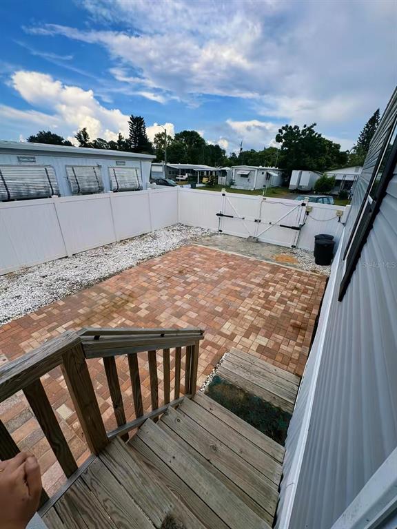 A wooden staircase leads down to a brick patio enclosed by a white vinyl fence — 2013 KEPNER DRIVE, HOLIDAY, FL