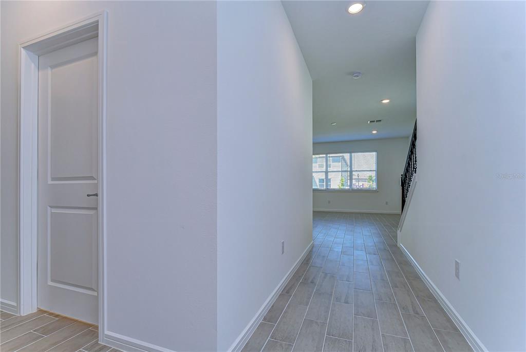 A hallway with light-colored tile flooring leads toward a room with windows and stairs — 17751 EVERLONG DRIVE, LAND O LAKES, FL