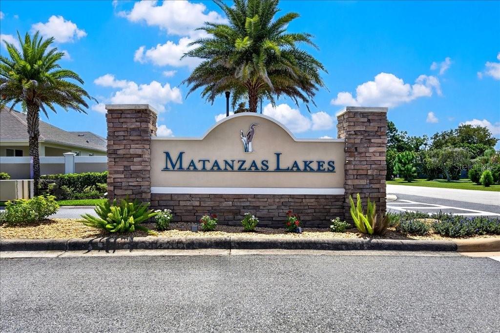 A stone monument sign for Matanzas Lakes stands outdoors under a blue sky with palm trees — 2 TIDEWAY TRAIL, PALM COAST, FL