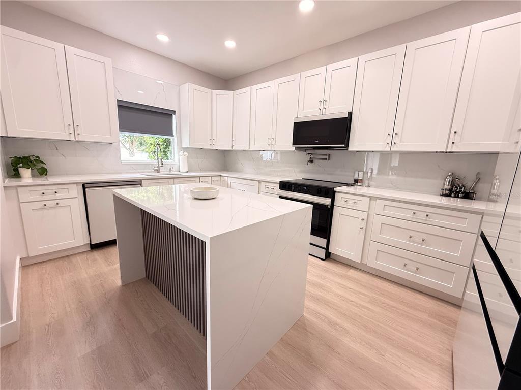 A modern kitchen features white cabinetry, a quartz-topped island, and light wood-look flooring — 5802 COQUYT DRIVE, MOUNT DORA, FL