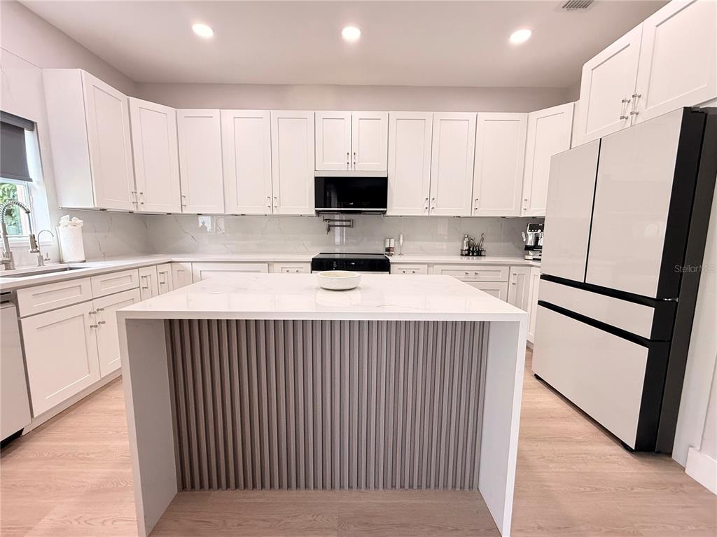 A modern kitchen features white cabinets, a marble-topped island with slatted detailing, and light flooring — 5802 COQUYT DRIVE, MOUNT DORA, FL