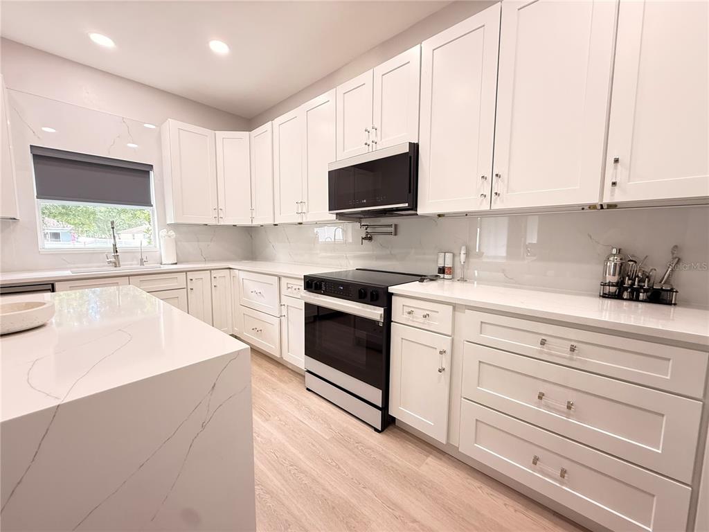 A modern kitchen features white shaker cabinets, quartz countertops, and stainless steel appliances — 5802 COQUYT DRIVE, MOUNT DORA, FL