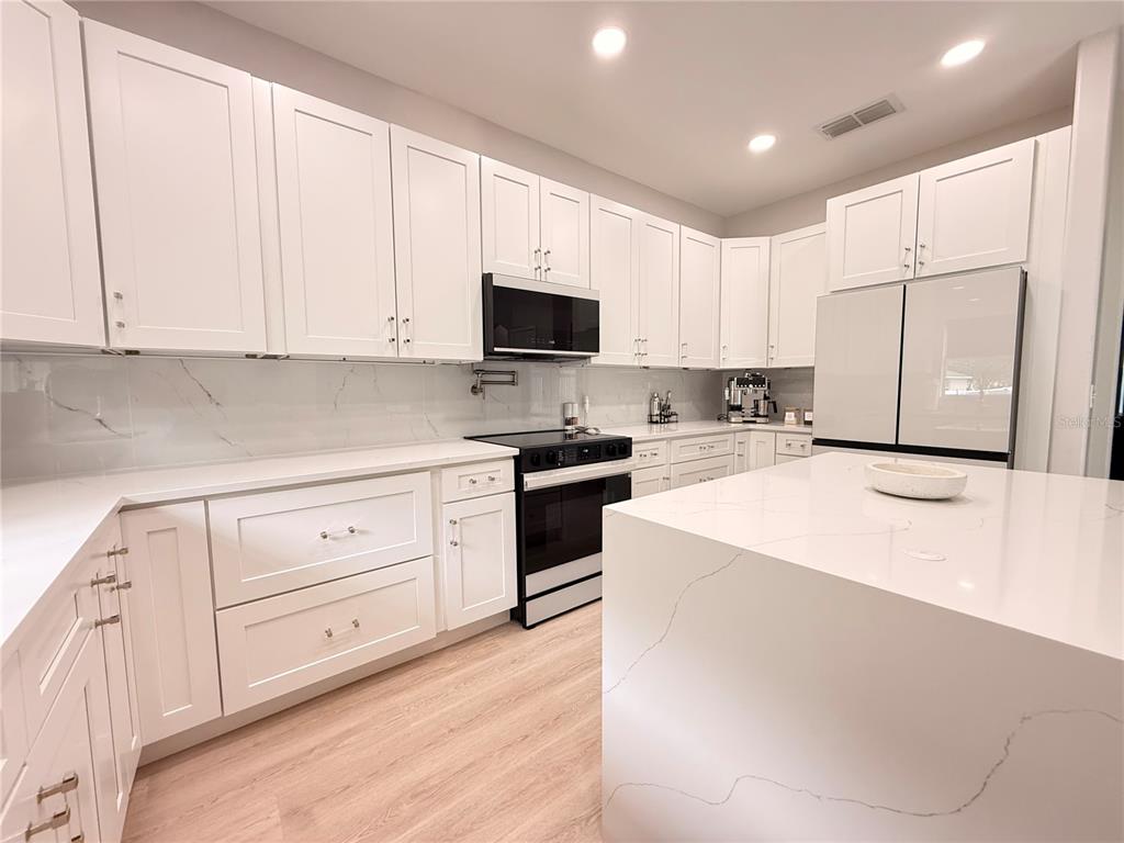 A modern kitchen features white shaker cabinets, quartz countertops, and stainless steel appliances — 5802 COQUYT DRIVE, MOUNT DORA, FL