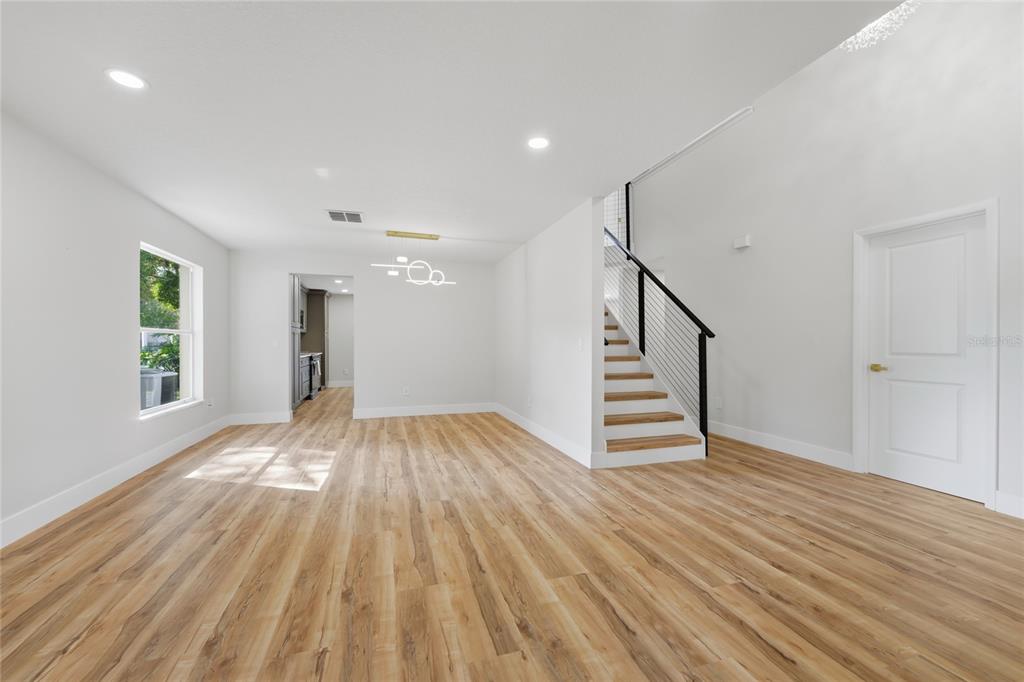 An open-concept room features light wood flooring, a modern staircase, and a doorway to a kitchen — 13044 BELLERIVE LANE, ORLANDO, FL