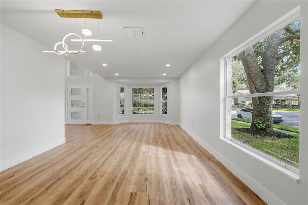 An empty living room with light wood-look flooring, a modern chandelier, and a bay window — 13044 BELLERIVE LANE, ORLANDO, FL