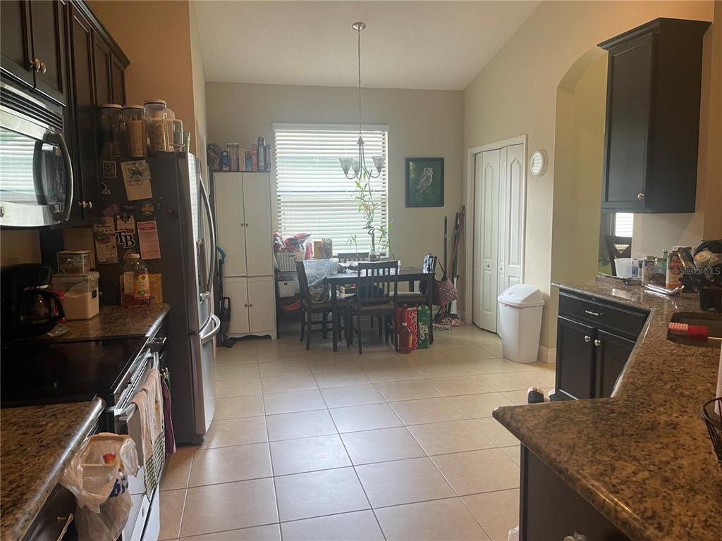 A kitchen with dark cabinets, granite countertops, and an adjacent dining area with a window — 824 VINO VERDE CIRCLE, BRANDON, FL