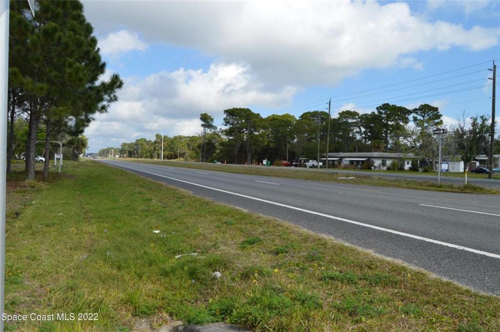 A paved road stretches past a grassy shoulder toward a line of trees and buildings — 3500 US HIGHWAY 1, MIMS, FL