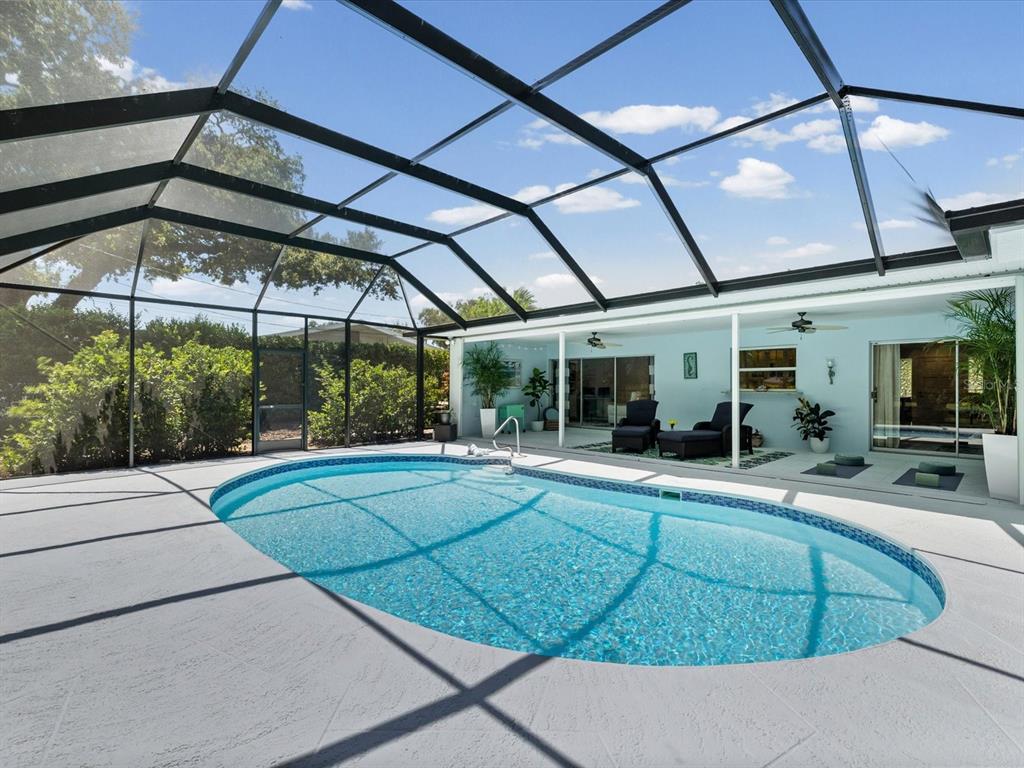 An oval swimming pool sits on a concrete patio enclosed by a black screen cage — 2285 WATROUS DRIVE, DUNEDIN, FL