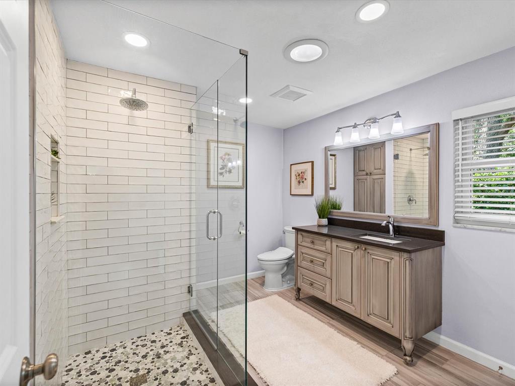 A bathroom features a glass-enclosed shower with subway tile, a vanity, and a toilet — 2285 WATROUS DRIVE, DUNEDIN, FL