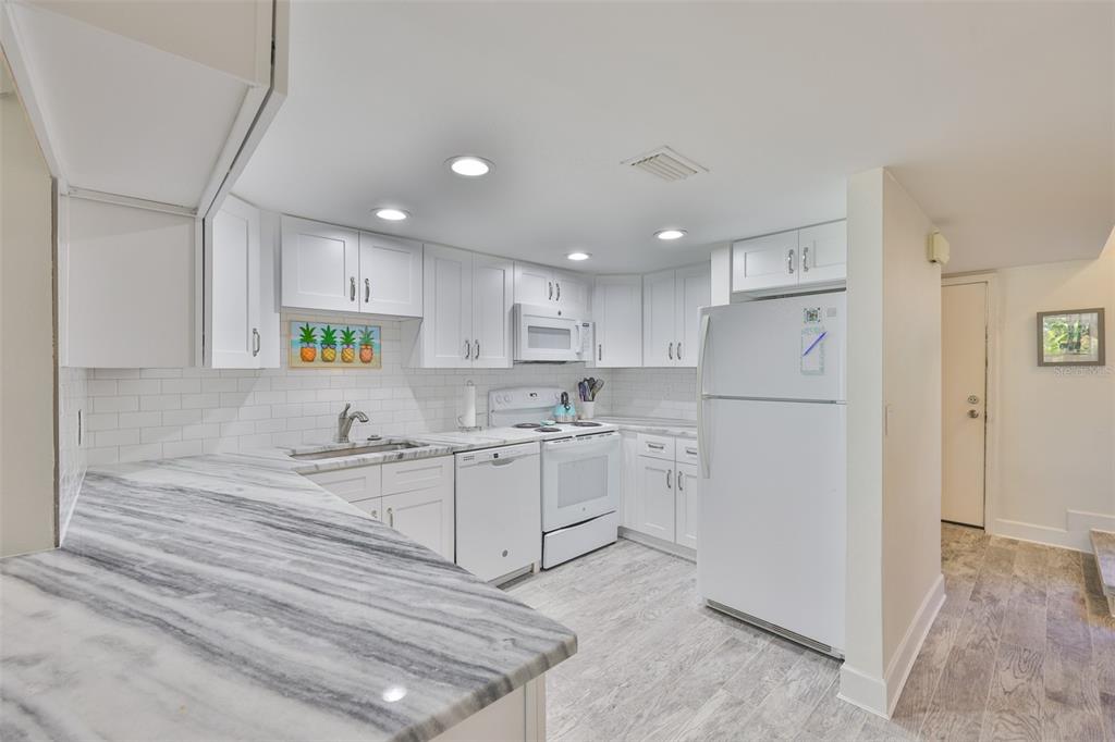 A white kitchen features marble-patterned countertops, subway tile backsplash, and light wood-look flooring — 1028 APOLLO BEACH BOULEVARD UNIT 8, APOLLO BEACH, FL