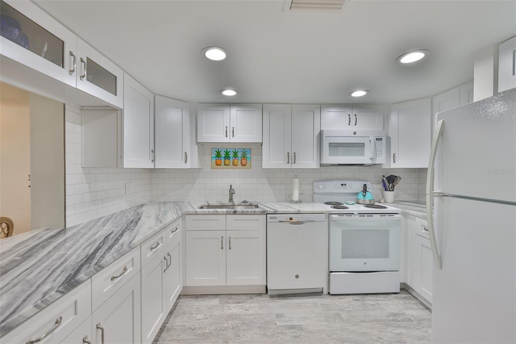 A kitchen features white cabinets, marble-patterned countertops, a white appliance suite, and subway tile backsplash — 1028 APOLLO BEACH BOULEVARD UNIT 8, APOLLO BEACH, FL