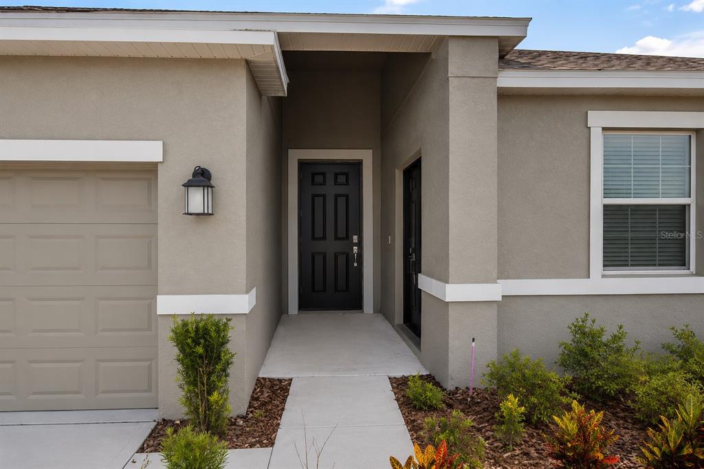 The exterior of a house features a tan stucco facade, a dark front door, and garage — 4249 BABBLING BROOK WAY, KISSIMMEE, FL