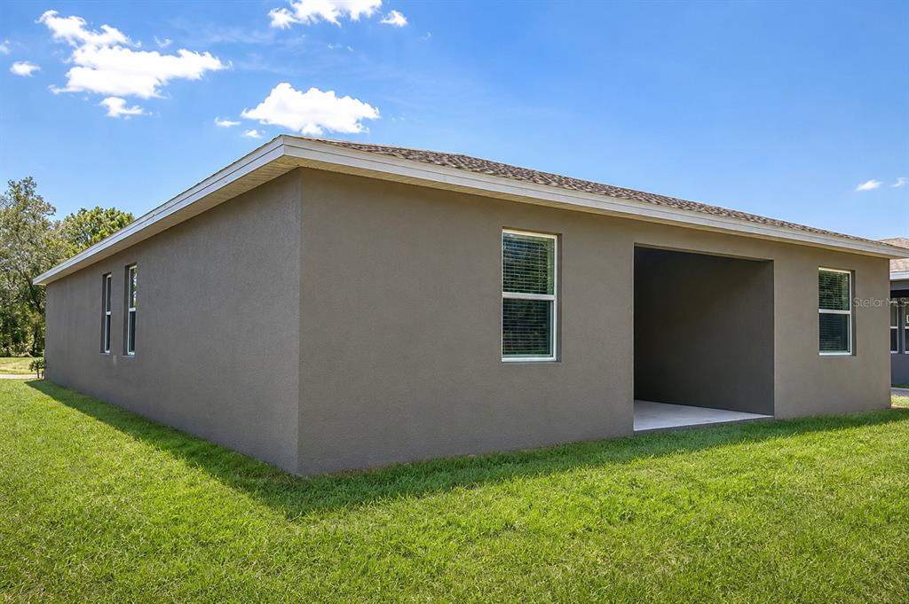 The exterior of a tan stucco house features a covered patio and several windows — 4249 BABBLING BROOK WAY, KISSIMMEE, FL