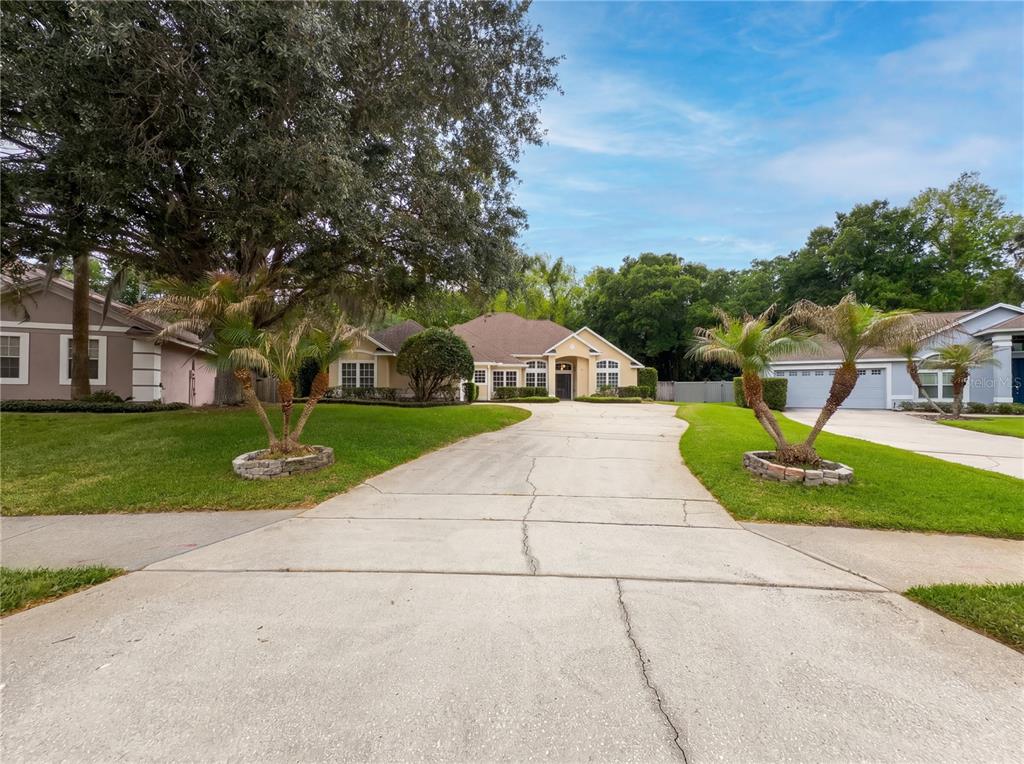 A single-story house with a concrete driveway, palm trees, and a large oak tree — 680 MACGLENROSS DRIVE, OVIEDO, FL