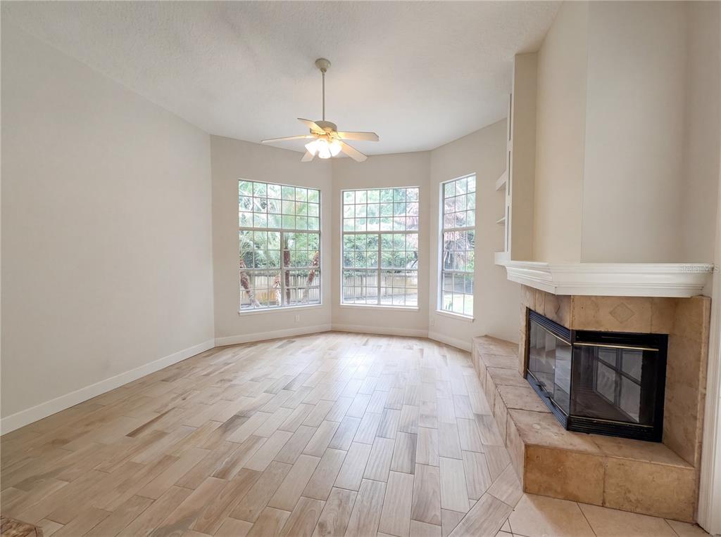 A living room with light wood-look tile flooring, a ceiling fan, and a corner fireplace — 680 MACGLENROSS DRIVE, OVIEDO, FL