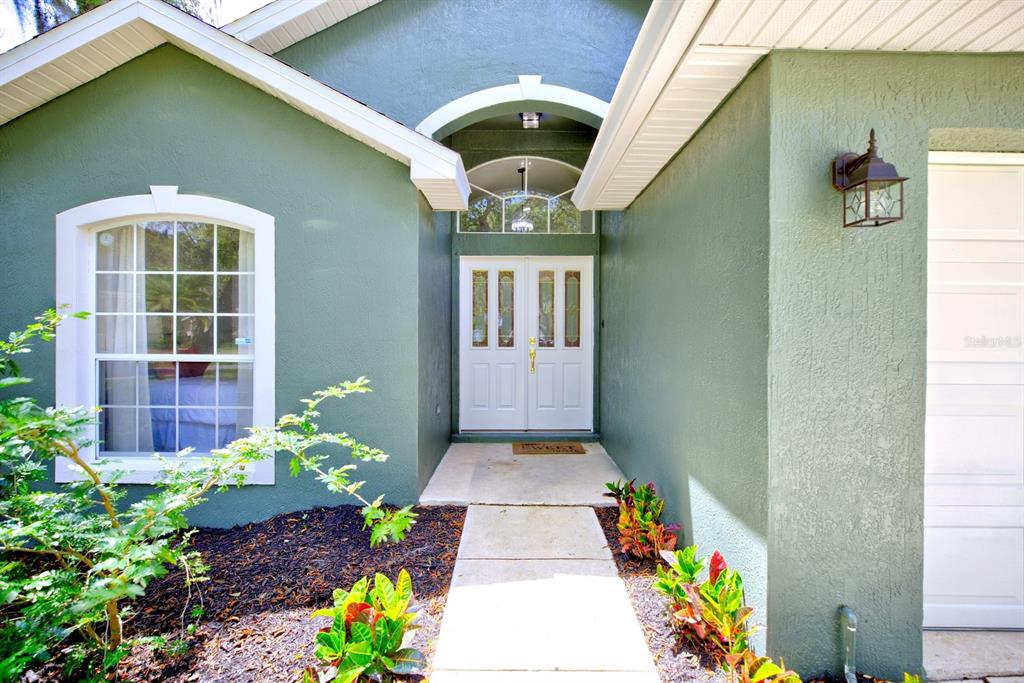 The exterior of a green house features a white double door entrance and a window — 1011 TEQUESTA TRAIL, LAKE WALES, FL