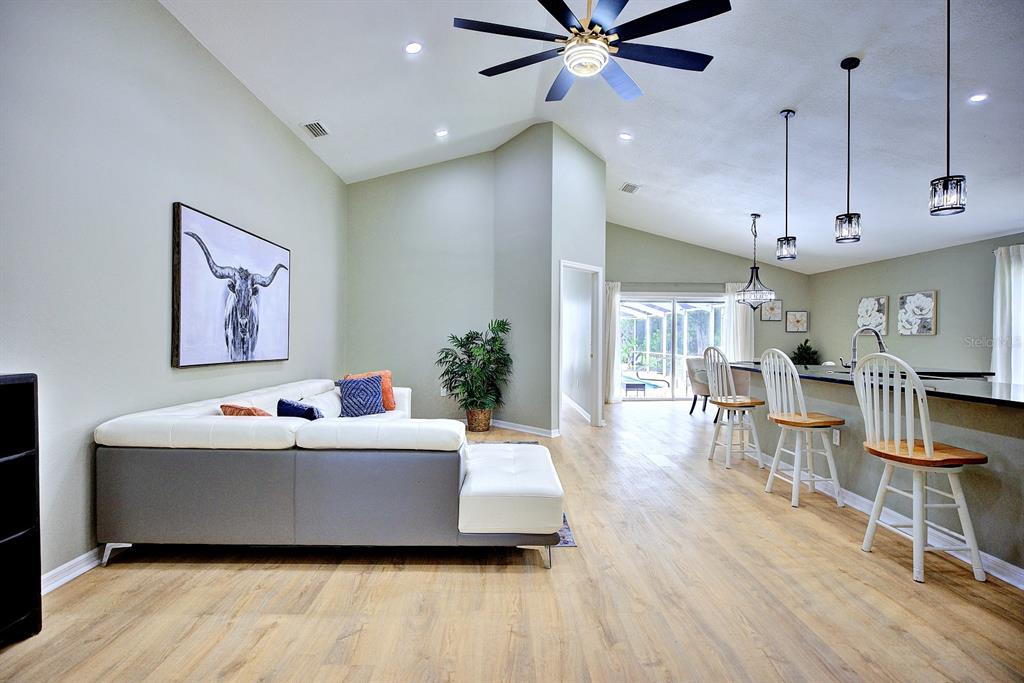 A living room with a white sectional sofa, wood-look flooring, and a kitchen breakfast bar — 1011 TEQUESTA TRAIL, LAKE WALES, FL