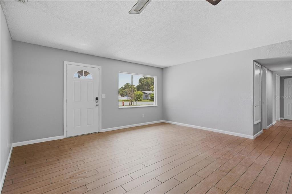 A living room with light gray walls, wood-look tile flooring, and a white front door — 1412 ORMOND AVENUE, APOPKA, FL
