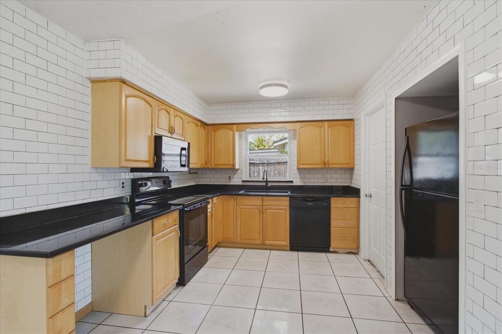 A kitchen with light wood cabinets, black countertops, white subway tile walls, and white tile floors — 1412 ORMOND AVENUE, APOPKA, FL