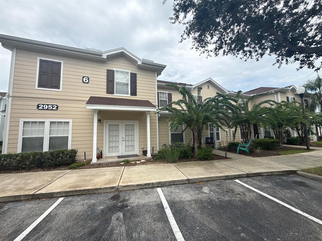 A two-story tan apartment building with double front doors and a concrete parking area — 2952 LUCAYAN HARBOUR CIRCLE UNIT 103, KISSIMMEE, FL