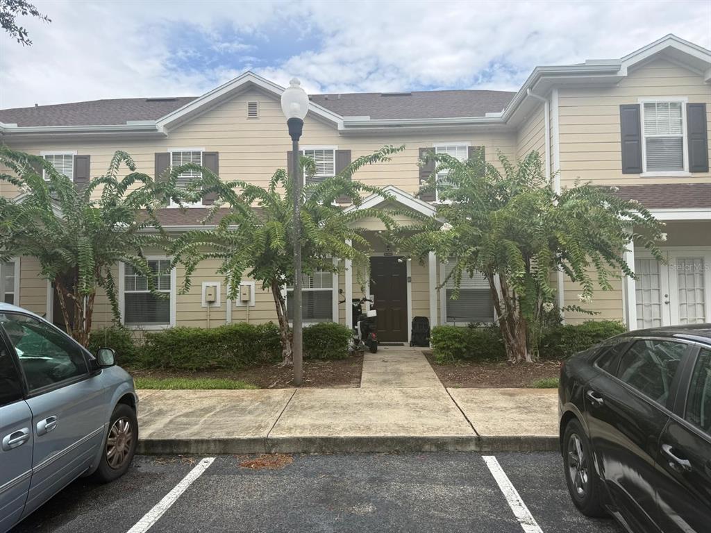 A two-story tan townhouse exterior features a central entrance, sidewalk, and two parked cars — 2952 LUCAYAN HARBOUR CIRCLE UNIT 103, KISSIMMEE, FL