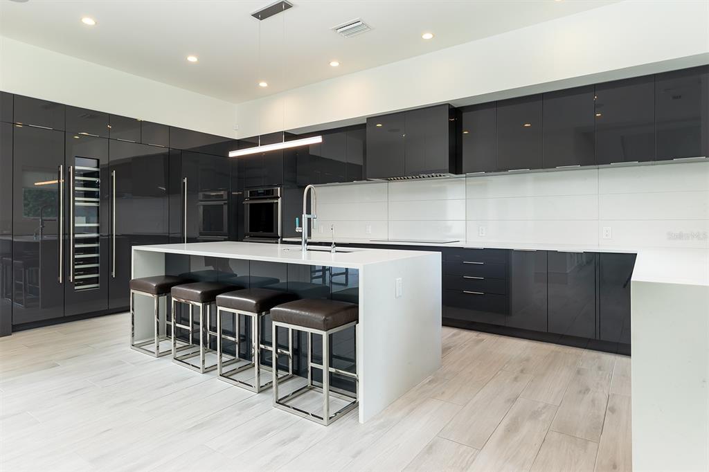 A modern kitchen features high-gloss black cabinetry, a white waterfall island, and light wood flooring — 231 CHELTON CIRCLE, WINTER PARK, FL