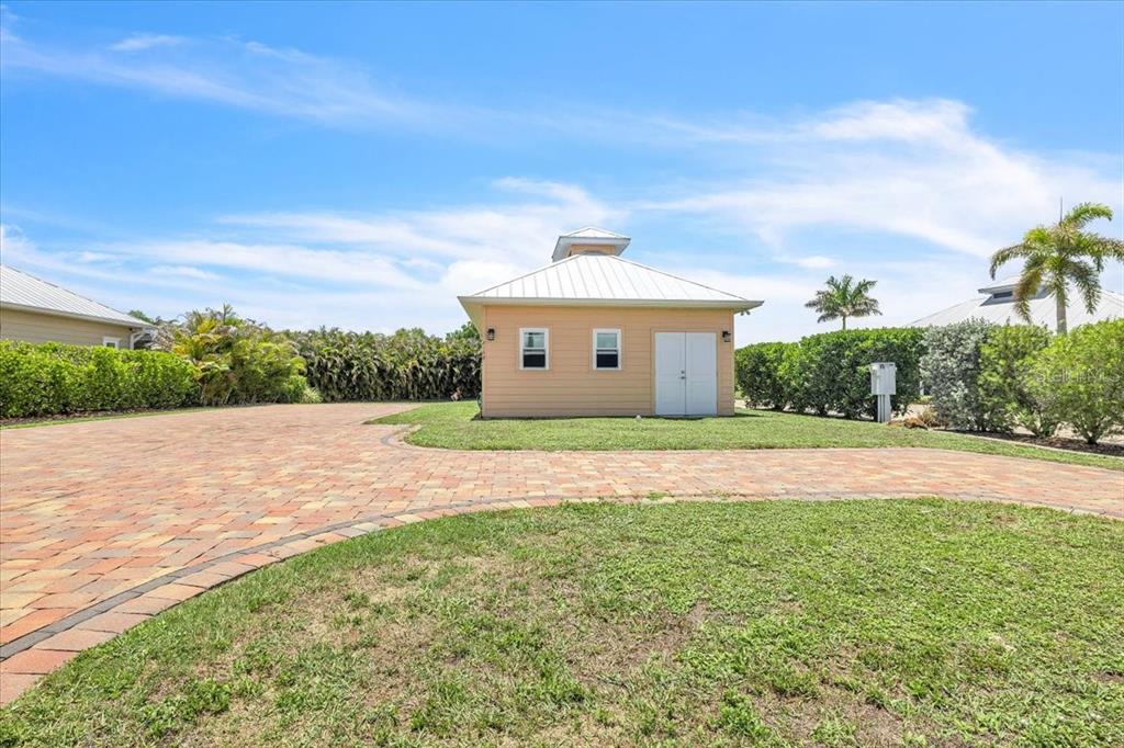 A detached tan shed with a metal roof sits on a paved driveway near landscaping — 8168 SW SAND CRANE CIRCLE, ARCADIA, FL