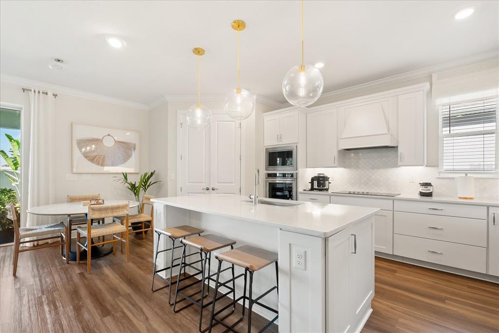 A modern white kitchen features stainless steel appliances, quartz countertops, and light wood-look flooring — 3208 SAILING PIER AVENUE, WINTER GARDEN, FL
