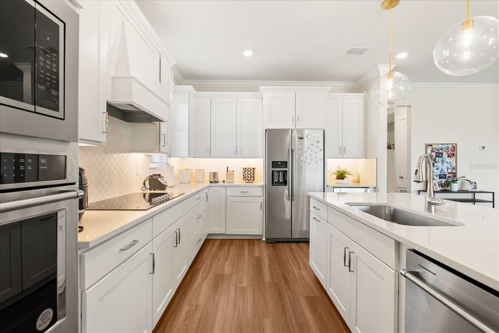 A modern kitchen features white cabinetry, a central island with bar stools, and dining area — 3208 SAILING PIER AVENUE, WINTER GARDEN, FL