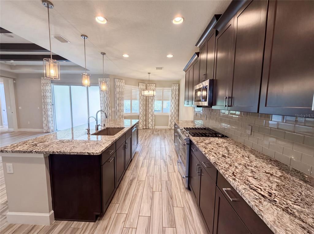 A kitchen features dark wood cabinets, granite countertops, a center island, and wood-look tile flooring — 1011 VICTORIA HILLS DRIVE S, DELAND, FL