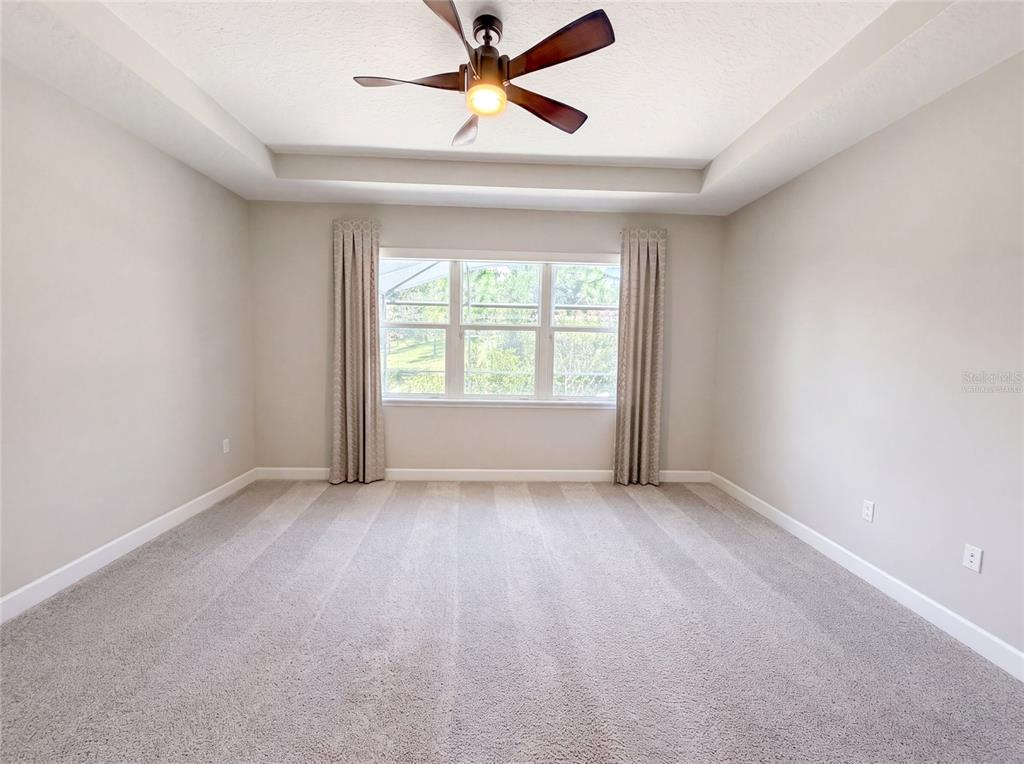 An empty bedroom features a tray ceiling, a ceiling fan, carpeted floors, and a window — 1011 VICTORIA HILLS DRIVE S, DELAND, FL